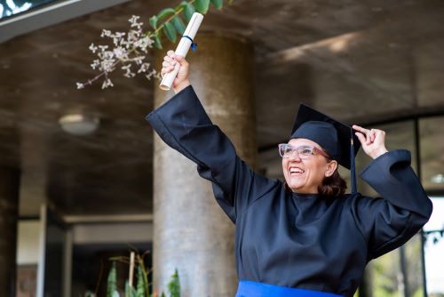 Woman proudly holds her diploma up while in cap and gown.